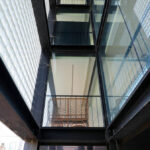 Casa Sacerdotal de São Martinho de Dume by André and António Fontes showcasing a symmetrical design with composite materials, extensive glass façades, metal and iron structural elements, steel and aluminium assemblies, and daylighting features creating reflective surfaces.