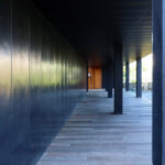 Casa Sacerdotal de São Martinho de Dume by André Fontes and António Fontes showcasing a symmetrical structure with wood planks, composite materials, concrete elements, metal accents, and hardwood finishes under natural daylight.