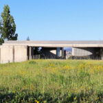 Projecto Homem by André and António Fontes showcasing a modern concrete structure set on a grassy land lot with expansive groundcover and plain surroundings.