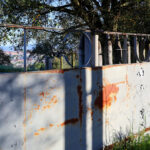 Projecto Homem by André Fontes and António Fontes showcasing a rusted metal chain-link fence with graffiti and wire mesh elements surrounding the structure.