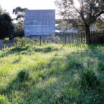 Projecto Homem by André and António Fontes showcasing a modern structure with a minimalist design set in a grassy meadow surrounded by a wooden fence and open pasture.