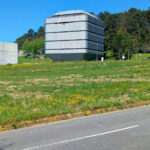 António Fontes’ Instituto para a Bio-Sustentabilidade at Universidade do Minho showcasing a high-rise corporate headquarters with a glass façade, green rooftop, and integrated urban design surrounded by grass and land lot.