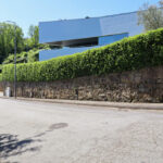 Eduardo Souto de Moura’s Casa em Oliveira do Douro showcasing a minimalist structure integrated into a sloped landscape with conifers, hedges, and carefully arranged shrubs.