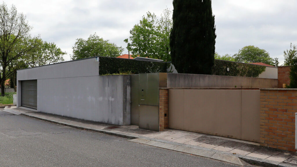 Eduardo Souto de Moura’s Casa na Senhora da Hora showcasing a minimalist concrete façade with composite material garage door, grey walls, and a shaded driveway.