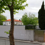 Eduardo Souto de Moura’s Casa na Senhora da Hora showcasing a modern residential concrete structure with composite material accents, surrounded by conifers, home fencing, and situated in a suburban area with trees.