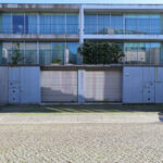 Eduardo Souto de Moura’s Casas Quinta da Avenida showcasing minimalist modern design with clean lines, concrete and glass façades, and integrated parking spaces featuring luxury and compact vehicles.