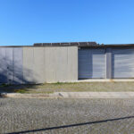 Eduardo Souto de Moura’s Casas Quinta da Avenida showcasing a minimalist concrete structure with composite material walls, a grey garage door, and a sloped land lot surrounding the building.