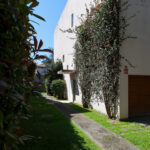 Eduardo Souto de Moura’s Duas Casas na Rua Beato Inácio de Azevedo showcasing minimalist walls, shaded yard areas, hedges, and shrubs surrounding the modern residential structures.