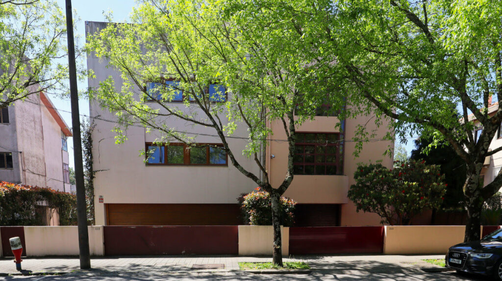 Eduardo Souto de Moura’s Duas Casas na Rua Beato Inácio de Azevedo showcasing minimalist walls, shaded yard areas, hedges, and shrubs surrounding the modern residential structures.