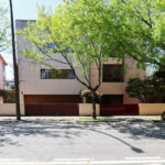 Eduardo Souto de Moura’s Duas Casas na Rua Beato Inácio de Azevedo showcasing minimalist modern design with shaded outdoor spaces and integrated parking areas featuring subcompact and executive cars.