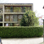 Eduardo Souto de Moura’s Edifício de Habitação Coletiva showcasing a residential apartment building with balconies, a driveway, and a subcompact car parked in front.
