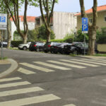 Eduardo Souto de Moura’s Edifício de Habitação Coletiva showcasing a modern residential building with clean lines, adjacent to a zebra crossing and road surface featuring cars and street lighting.