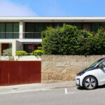 Eduardo Souto de Moura’s Habitações Unifamiliares showcasing minimalist modern residential design with clean lines, concrete façades, and integrated driveway featuring a parked subcompact car with visible car door and rear-view mirror.