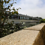 Eduardo Souto de Moura’s Habitações Unifamiliares showcasing a concrete and composite material façade with shaded walkways, daylighting elements, and surrounding hedges during daytime.