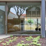 Eduardo Souto de Moura’s residential building showcasing a concrete structure with a composite material door, hardwood elements, glass panels for daylighting, and a shaded entrance design.