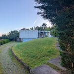 Jean Pierre Porcher, Joaquim Oliveira, and Albino Freitas’ design of House 1 to 6 showcasing modern residential architecture with landscaped gardens, sloped lawns, conifer shrubs, and expansive yard spaces under daytime lighting.