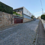 House 1 to 6 designed by Jean Pierre Porcher, Joaquim Oliveira, and Albino Freitas, showcasing modern residential architecture with brick and flagstone driveways, sloped terrain, and a suburban setting featuring sidewalks and a tar road surface.