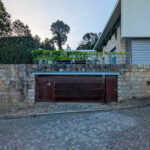 House 1 to 6 designed by Jean Pierre Porcher, Joaquim Oliveira, and Albino Freitas featuring a combination of brick, concrete, and stone walls with a driveway leading to a modern garage with a sleek garage door.