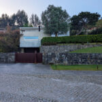 Loteamento D. Antónia Amorim by Jean Pierre Porcher, Margarida Oliveir, and Albino Freitas showcasing a concrete structure with a stone wall and neatly trimmed hedge.