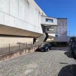 Jorge Nuno Monteiro’s Pavilhão Desportivo Municipal de Santo Tirso showcasing a brutalist concrete structure with composite materials, prominent stairs with handrails, and ample daylighting.