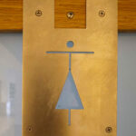 Jorge Nuno Monteiro’s Pavilhão Desportivo Municipal de Santo Tirso showcasing a triangular brass symbol mounted on a plywood surface as part of the building’s modern architectural design.