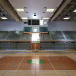 Jorge Nuno Monteiro’s Pavilhão Desportivo Municipal de Santo Tirso showcasing a spacious sports hall with hardwood basketball court, basketball hoops, large windows providing ample daylighting, and an open arena layout.