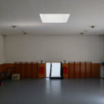Jorge Nuno Monteiro’s Pavilhão Desportivo Municipal de Santo Tirso interior showcasing wood flooring with varnish finish, high ceiling with integrated lighting, and spacious hall design.