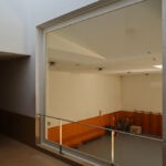 Jorge Nuno Monteiro’s Pavilhão Desportivo Municipal de Santo Tirso showcasing an interior with wood-stained walls and flooring, large glass panels allowing natural daylighting, and a detailed wooden ceiling structure.