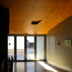 Jorge Nuno Monteiro’s Pavilhão Desportivo Municipal de Santo Tirso showcasing an interior with wood flooring and ceiling, warm brown wood stain, hardwood elements, modern lighting fixtures, and large glass panels.