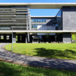 OPERA | Design Matters' Escola de Medicina, Universidade do Minho, showcasing a modern campus building with composite material façade, extensive daylighting through large windows, integrated shading elements, and surrounding green lawn and yard spaces.
