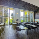 OPERA | Design Matters' Escola de Medicina, Universidade do Minho, showcasing a modern glass façade with extensive daylighting, shaded cafeteria space featuring contemporary furniture and chairs, and a spacious dining area with visible ceiling structures.