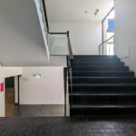 OPERA | Design Matters' Escola de Medicina, Universidade do Minho interior showcasing black composite flooring, grey metal handrails, modern stairs, and a sleek ceiling design.