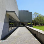 Pedro Ramalho and Luis Ramalho’s Casa das Artes showcasing a concrete and composite material façade with expansive shaded public spaces, landscaped lawn, and modern urban design elements during daytime.