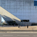 Rem Koolhaas’s Casa da Música showcasing a daytime view of the commercial building with a striking concrete brutalist architecture, featuring angular composite material surfaces and innovative structural engineering.