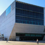 Rem Koolhaas’s Casa da Música showcasing a blue composite material façade with brutalist architectural elements, featuring a cantilevered structure in a metropolitan commercial urban setting during daytime.