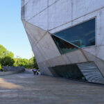 Rem Koolhaas’s Casa da Música showcasing a triangular concrete structure with composite materials, featuring brutalist architecture elements, extensive daylighting, and sharp shadows during daytime.