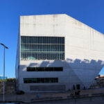 Rem Koolhaas’s Casa da Música showcasing a daytime view of the commercial building with a striking concrete brutalist architecture, composite materials, and complex geometric forms in an urban metropolitan setting.