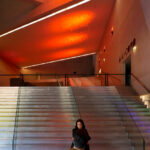Rem Koolhaas’s Casa da Música showcasing its dramatic interior lighting, angular ceiling design, winding stairs with sleek handrails, and dynamic shadows at night.