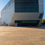 Rem Koolhaas’s Casa da Música showcasing a brutalist concrete commercial building with composite materials, featuring bold geometric forms and urban design elements under a clear blue daytime sky.