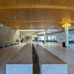 Ricardo Vieira de Melo and Eduardo Rebelo’s Complexo Pedagógico II at Universidade do Minho showcasing symmetrical wood flooring, composite material ceiling, tiled floors, and evenly spaced columns with modern lighting fixtures.