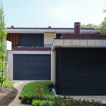 Unknown Architect’s Villa Rua de José de Carvalho showcasing a modern design with a concrete and composite material façade, featuring a garage door, gated driveway, and shaded courtyard area.
