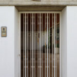 Unknown Architect’s Villa Rua do Padrão showcasing a modern home entrance with a grey composite wood gate, metal and iron details, concrete walls, and ample daylighting.