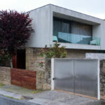 Unknown Architect’s Villa Tv. Cavada showcasing a modern concrete residential home with a sloped driveway, balcony, and surrounding walls in a residential area.