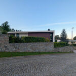 Unknown Architect’s Casas Rua Calvelo de Cima showcasing a modern farmhouse with a concrete driveway, stone wall, flagstone walkway, neatly trimmed hedge, and landscaped surroundings.