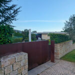 Unknown Architect’s Casas Rua Calvelo de Cima showcasing a modern stone and concrete wall with landscaped garden, shaded driveway, walkway, backyard, and neatly trimmed hedge.