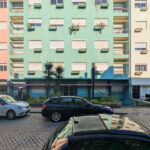 Colorful Buildings of Rua António José da Costa showcasing a vibrant urban design with mixed-use apartment and commercial buildings, featuring automotive parking lights and various vehicles including family cars, luxury vehicles, and subcompact cars.