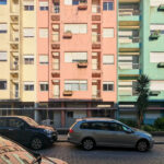 Colorful residential and commercial buildings of Rua António José da Costa featuring vibrant façades, mixed-use structures, and visible automotive parking lights in a metropolitan neighborhood.