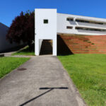 Unknown Architect’s Escola de Economia e Gestão, Universidade do Minho showcasing a modern composite material façade integrated into a sloped urban design with surrounding lawn, shade, and shadow elements.