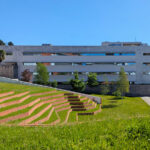 Unknown Architect’s Escola de Engenharia I at Universidade do Minho showcasing a modern campus building with a sloped lawn, landscaped yard, and paved walkways surrounded by green grass and open land.