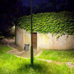 Unknown Architect’s Shower House Parque da Cidade showcasing a modern structure with garden landscaping, shaded backyard, and subtle night landscape lighting highlighting green shrubs and leaves.